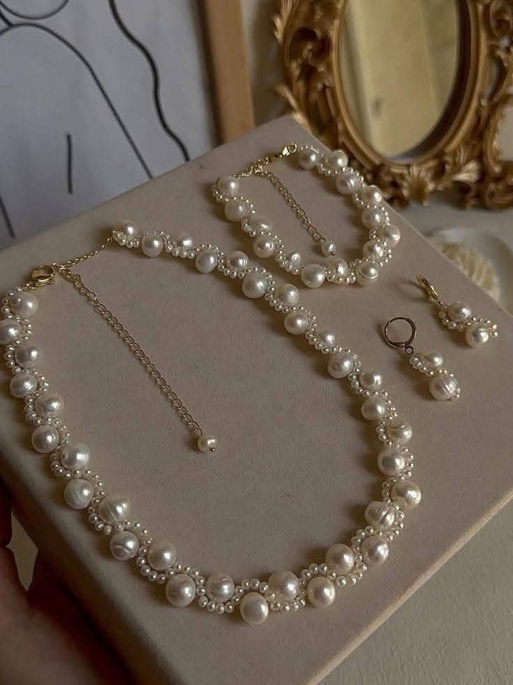 Champagne gold jewelry resting on aged handwritten letters beside a white rose and loose pearls