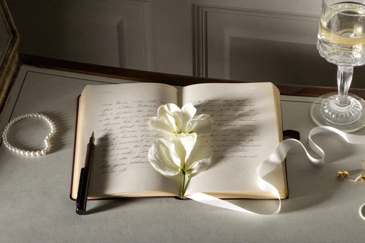 An open handwritten journal with pressed flowers, a fountain pen, pearls and silk ribbon in dawn light