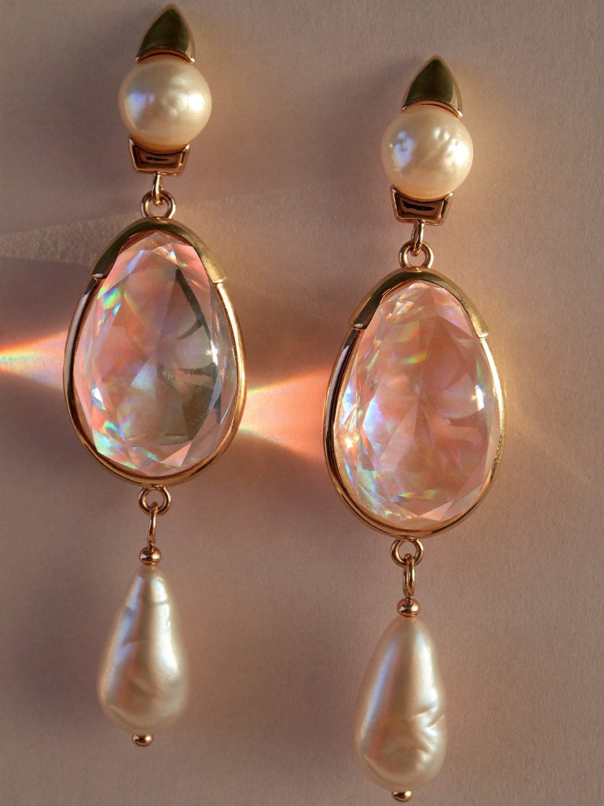 Pearl drop earrings in gold settings catching prismatic dawn light